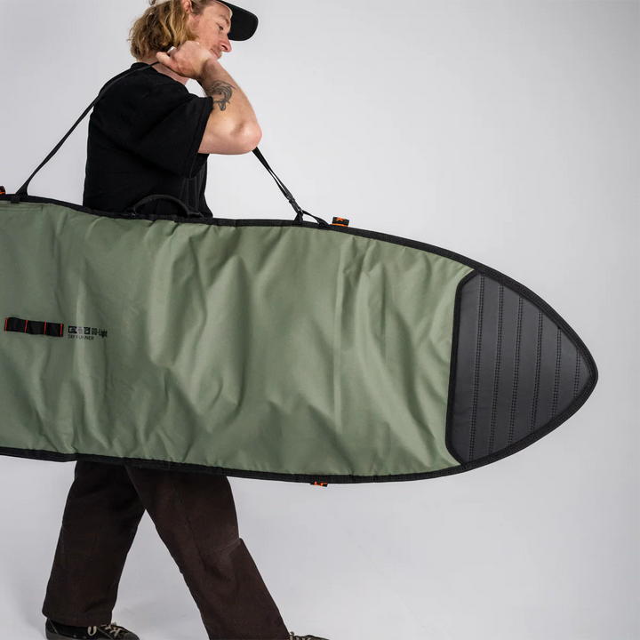 Person holding a green and black surfboard bag against a white background