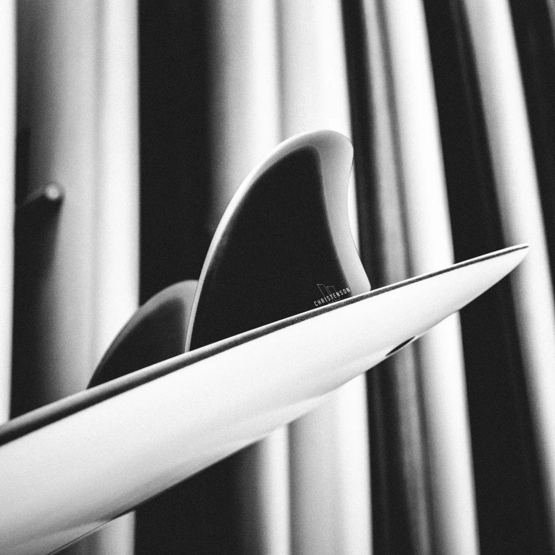 Close-up of a surfboard tail with black fins and a blurred background