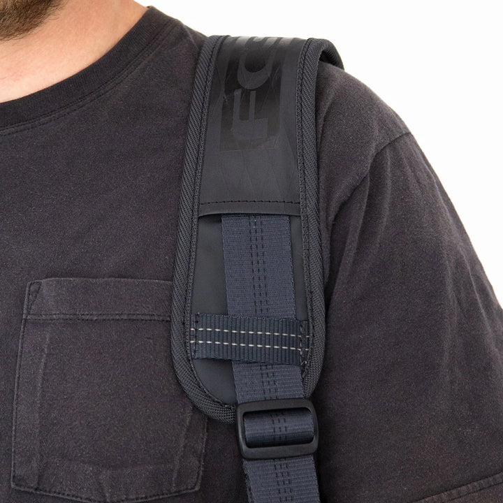 Close-up of person wearing a black FCS surfboard bag strapped over the shoulder with a visible brand logo on a white background
