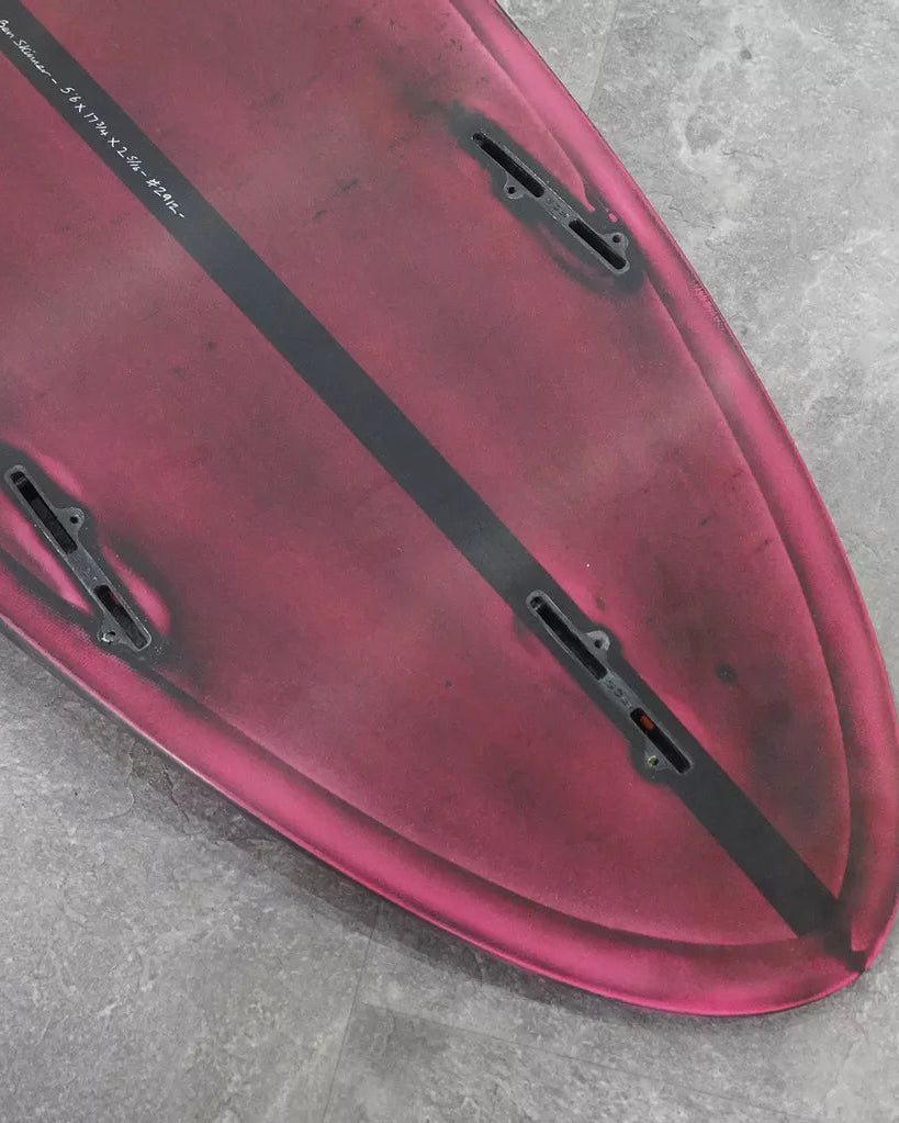 Close-up of a red surfboard with black stripe on a grey surface