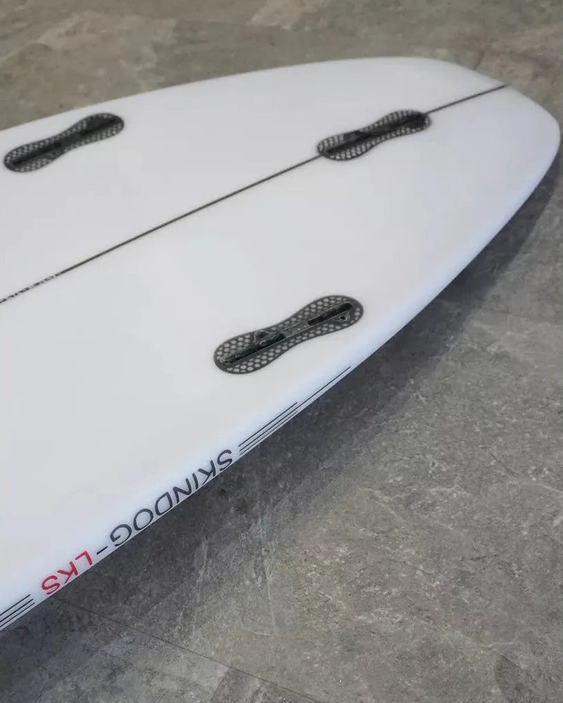 Close-up of a white surfboard with black fin boxes on a grey surface