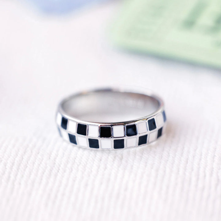 Silver ring with black and white checkered pattern on a textured surface