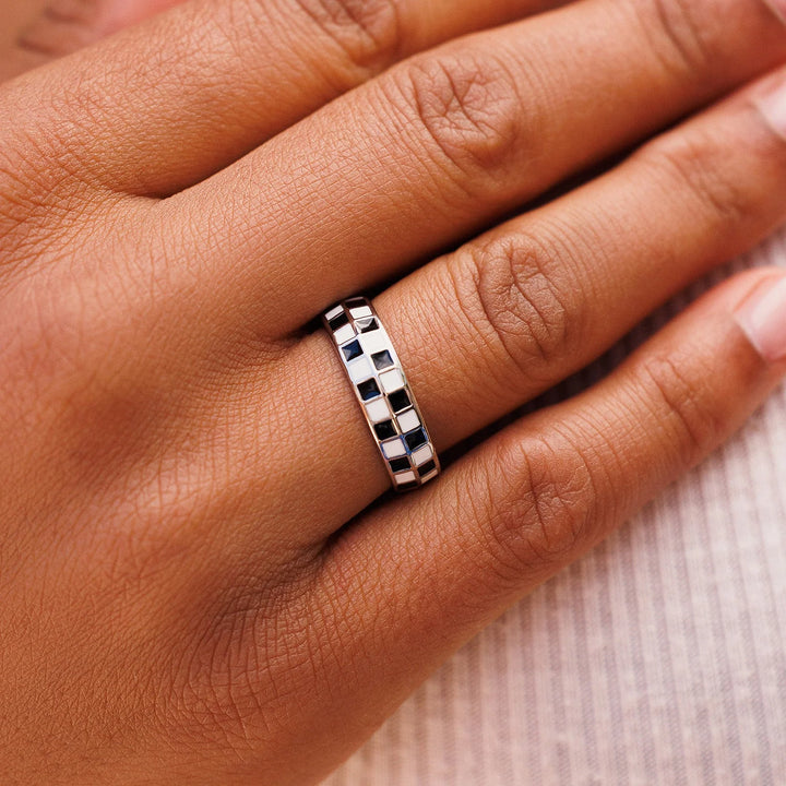 Close-up of a hand wearing a silver checkered ring on a neutral background