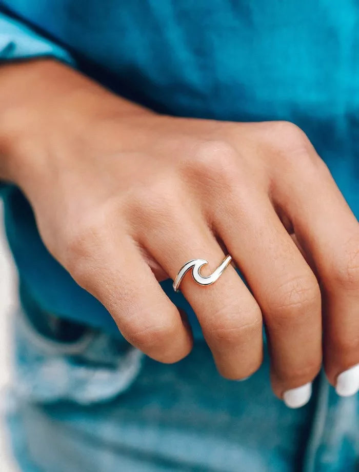 Hand wearing a silver wave-shaped ring with a blue fabric background