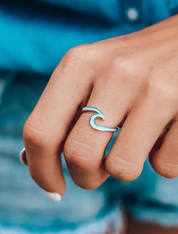 Close-up of a hand wearing a silver wave-shaped ring against a blue blurred background