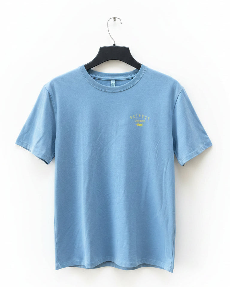 A light blue crewneck t-shirt hanging on a black hanger against a white background. The shirt features a small yellow graphic on the left chest that reads 'SKINDOG SURFBOARDS'.